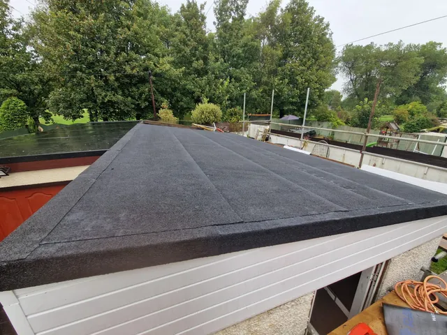 A garage flat roof re-covered by Pro Roofing in new mineral felt, with new white fascia boards along the edge and trees behind