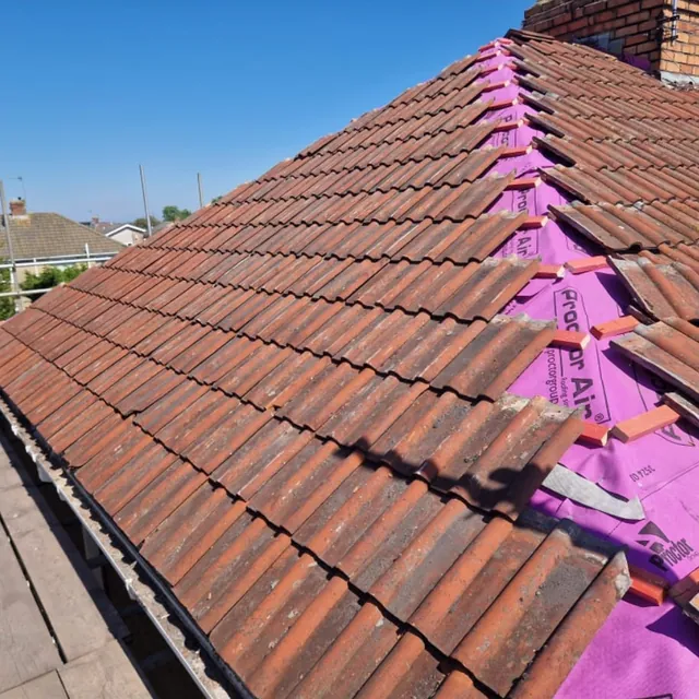 Stage four of the re-roof: clay tiles being laid back over the new membrane and battens beside the chimney