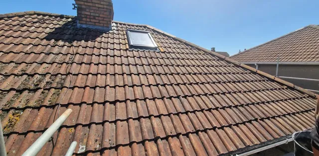 The same kind of roof once finished: clay tiles laid around a brick chimney and a roof window by Pro Roofing