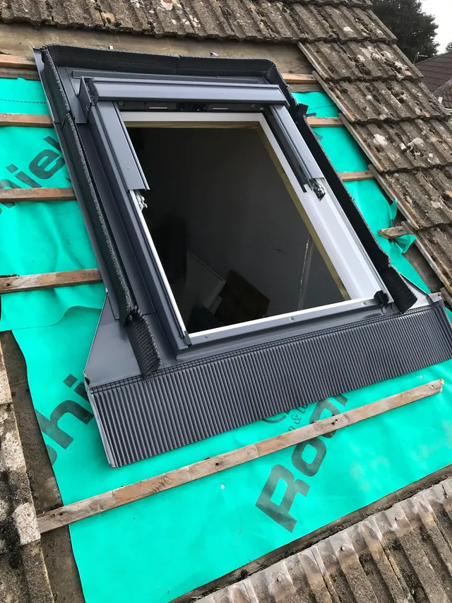 A roof window part-way through being fitted by Pro Roofing, with its frame and grey flashing kit in place over new green roofing membrane